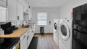 Una cocina moderna con armarios blancos, encimera de madera, refrigerador negro y lavadora.