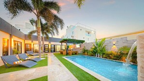 Uma área de piscina moderna ao ar livre, com espreguiçadeiras, um pequeno espaço de estar e uma cascata.