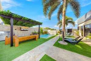 Ein Garten mit Pool, Sitzgelegenheiten und einer mit Grünpflanzen bewachsenen Pergola.