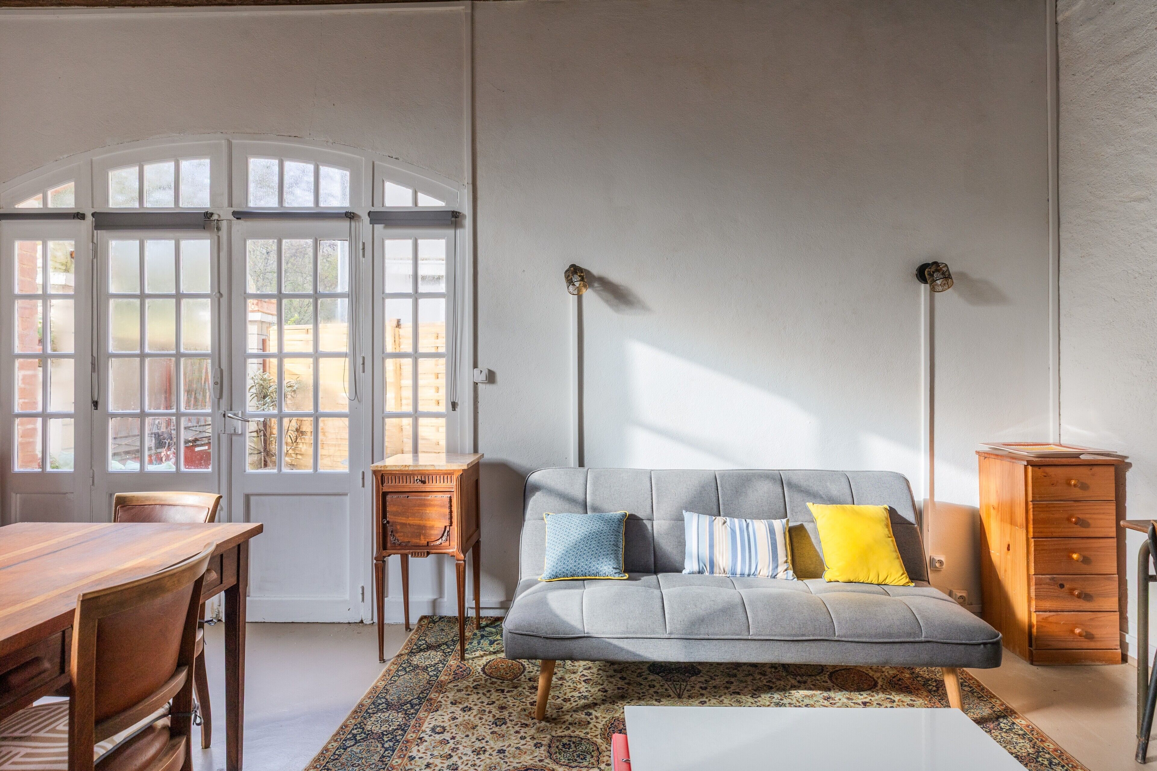 Una habitación con sofá, una mesa de madera, alfombra estampada y un armario.