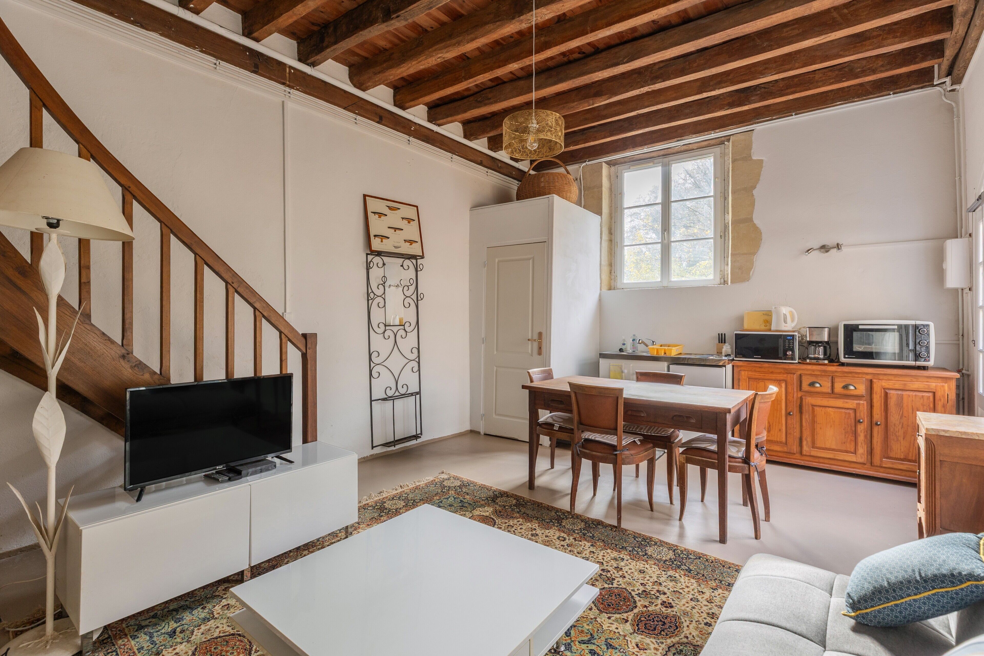 A living room with a TV, white sofa, and a dining area with wooden chairs and a table.