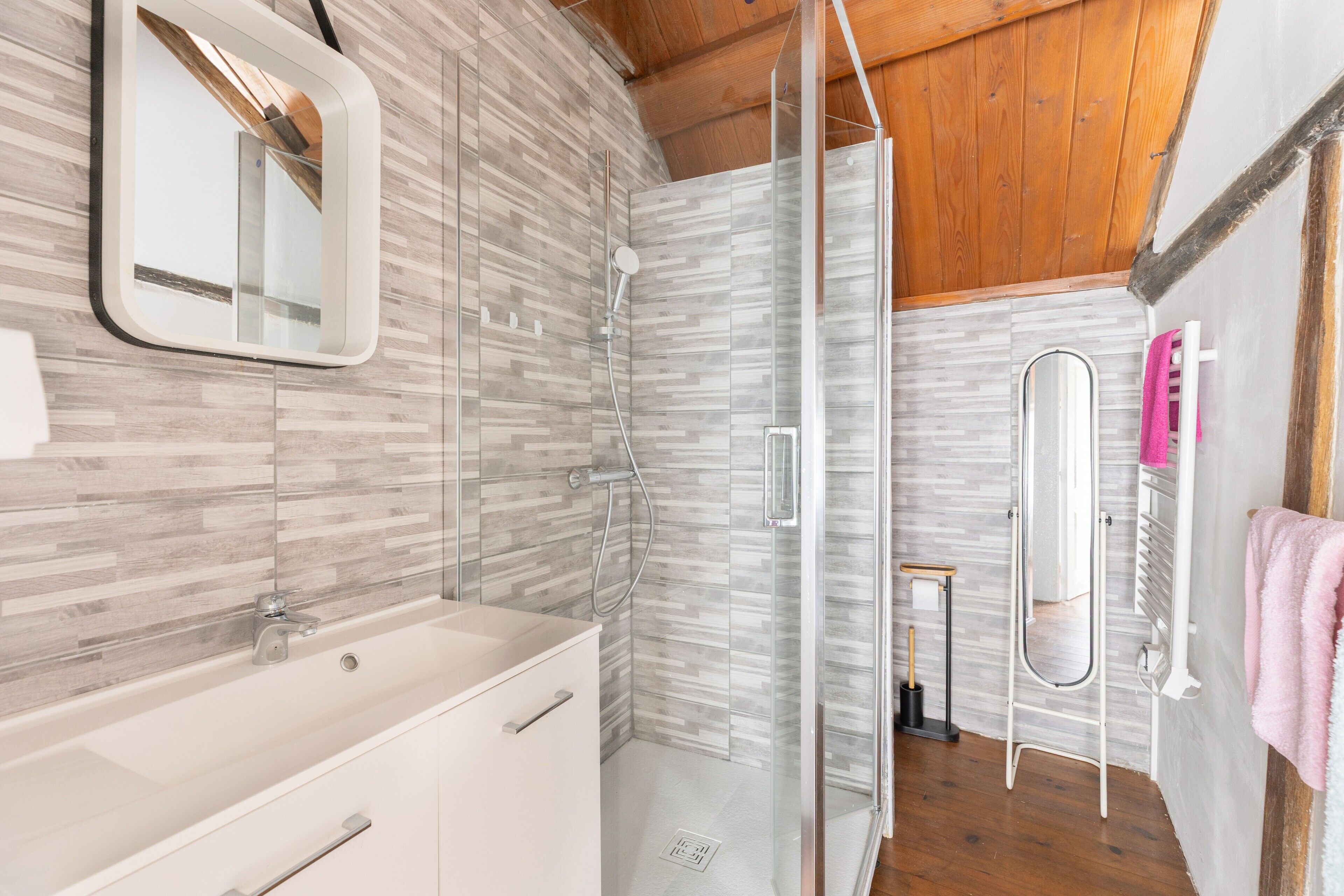 A modern bathroom with a glass shower enclosure, a white sink, and a mirror.