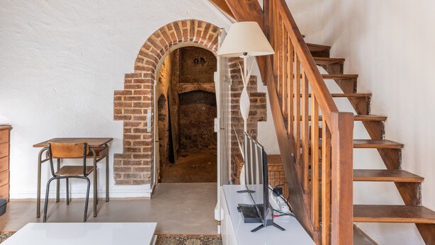 Un escalier avec des marches en bois et une rampe en métal, menant à une arche en briques.