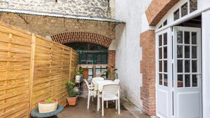 Une terrasse avec une table et des chaises, une clôture en bois et une arche en briques.