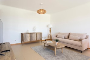 A modern living room with a wooden coffee table, a beige sofa, a wooden cabinet, and a floor lamp. - Snazzy Varandas do Castelo - One Bedroom Apartment Sleeps 2 Person (Albufeira)