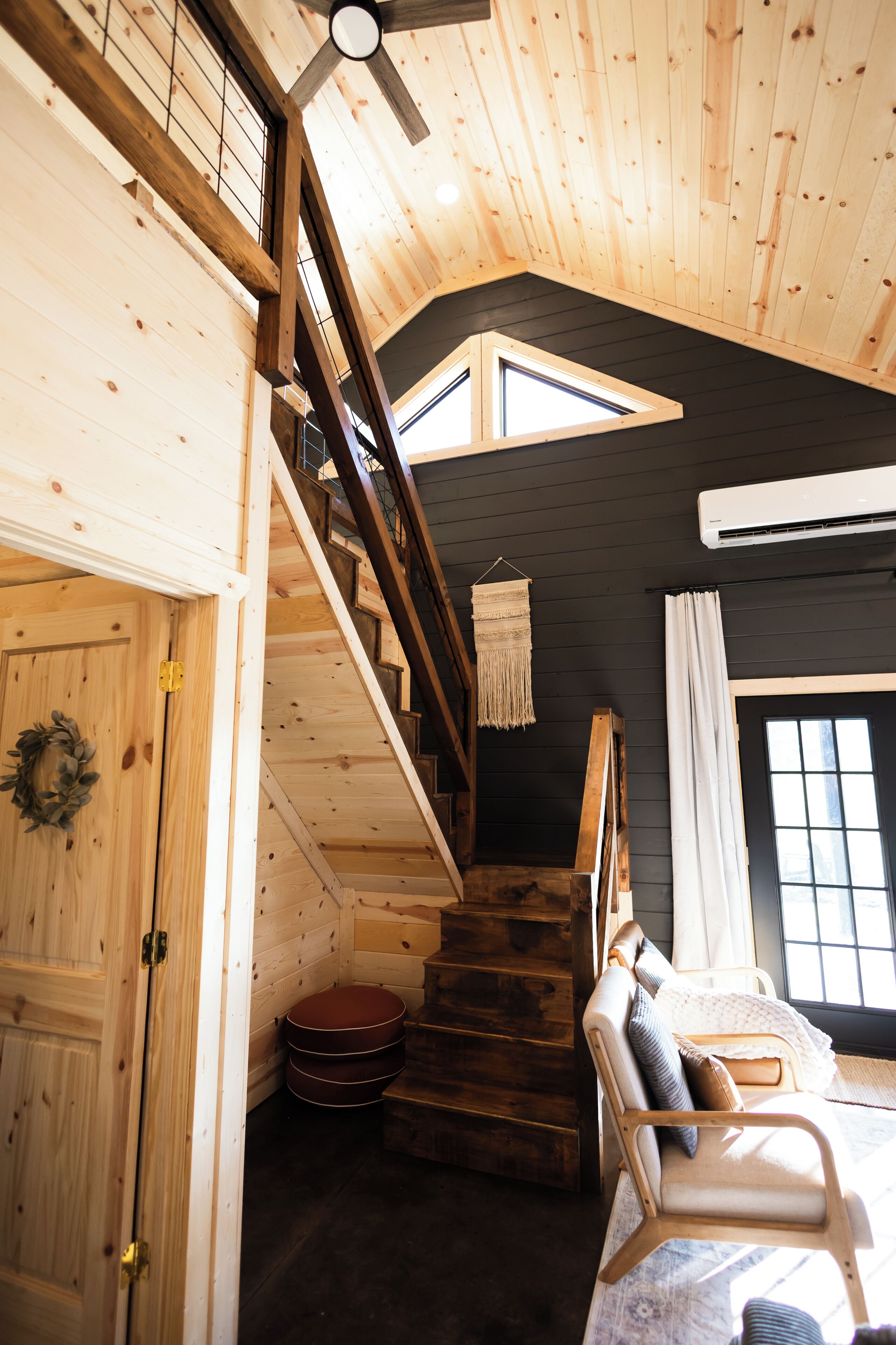 A wooden interior with a staircase, a bed with pillows, and a window.