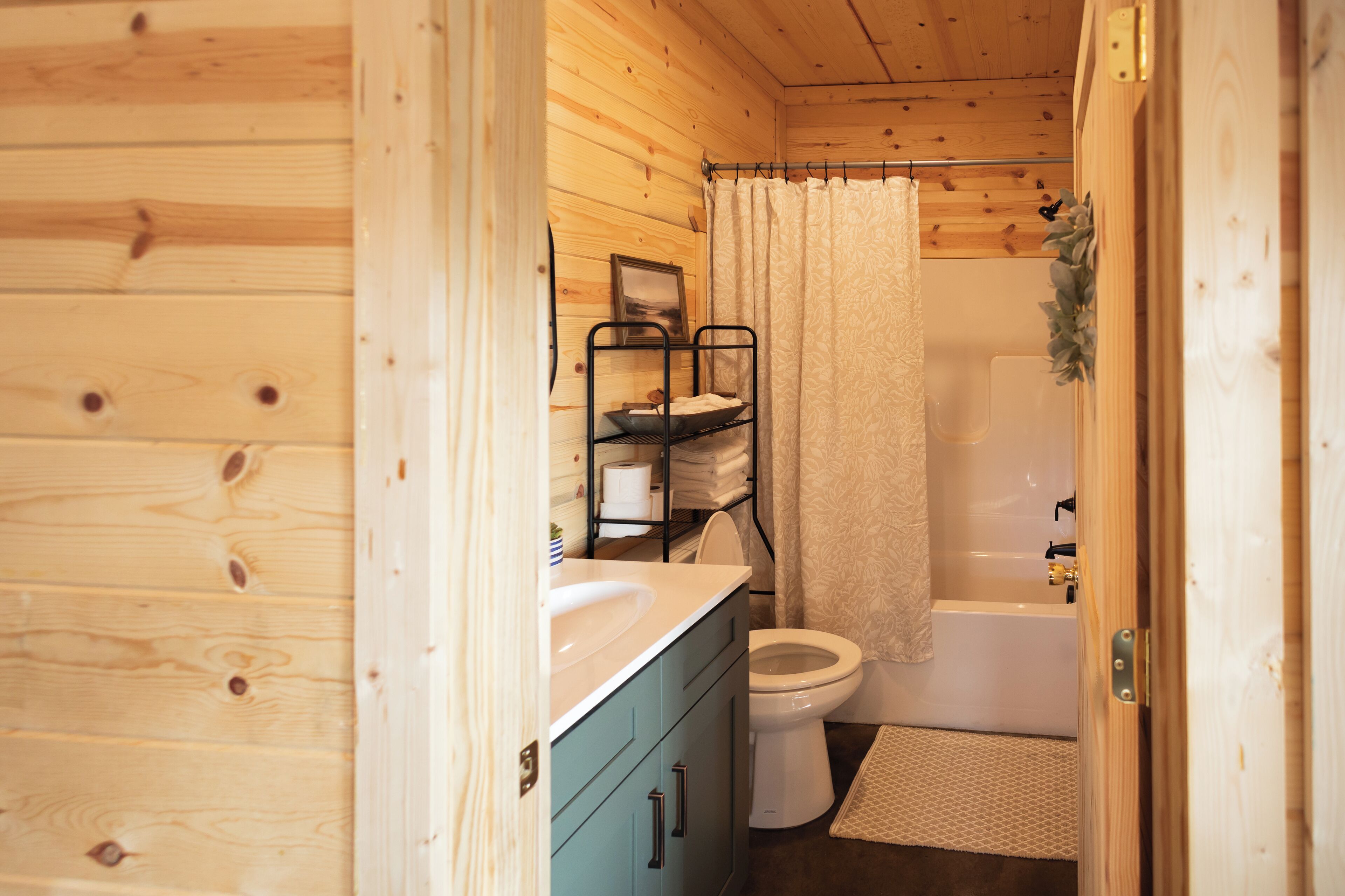 A wooden cabin bathroom with a white toilet, a bathtub, and a sink.