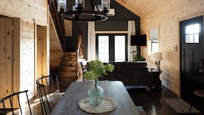 Ein Holzinterieur mit einem Esstisch, Stühlen, einer Vase mit Blumen, einer Treppe und einem Fernseher.