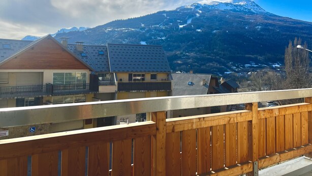 Een balkon met uitzicht op een berg en omliggende gebouwen.