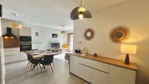 Een moderne keuken met een eethoek, met een centraal kookeiland, inbouwoven en een groot raam dat voor natuurlijk licht zorgt.