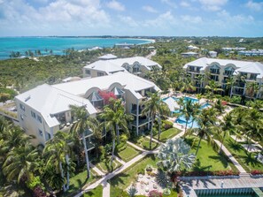 A resort with multiple buildings, a central pool, and a view of the ocean. - Ground Floor Yacht Club Condo E1 - Sunset Views, BBQ, Walk to Beach and Dining (Providenciales)