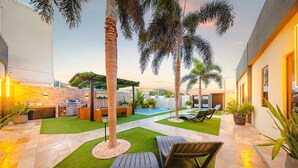 En moderne udendørs terrasse med swimmingpool, liggestole og grillområde.