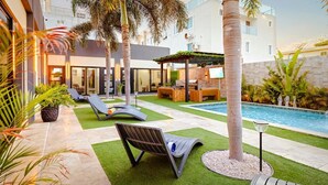 Et moderne udendørs poolområde med liggestole, grillfaciliteter og en overdækket siddeplads.