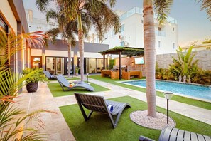 A modern outdoor pool area with lounge chairs, a barbecue setup, and a covered seating area. - New Sea La Vie Suite # 5 |2BR|1BR W. Pool&Jacuzzi (Noord)