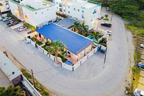 A multi-story hotel with a blue roof, surrounded by a parking area and palm trees. - New Sea La Vie Suite # 5 |2BR|1BR W. Pool&Jacuzzi (Noord)