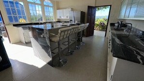 Une cuisine spacieuse dotée d’un grand îlot central, de tabourets de bar et offrant une vue sur l’extérieur.