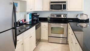 A kitchen with white cabinets, stainless steel appliances, and a black countertop. - Beachfront Perdido Key Condo | Private Balcony (Pensacola)