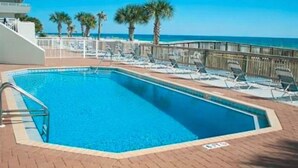 A rectangular pool with a metal ladder, surrounded by lounge chairs and a wooden deck. - Beachfront Perdido Key Condo | Private Balcony (Pensacola)