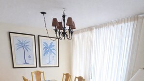 A dining area with a glass table, wicker chairs, a beach-themed rug, and framed artwork on the wall. - Beachfront Perdido Key Condo | Private Balcony (Pensacola)