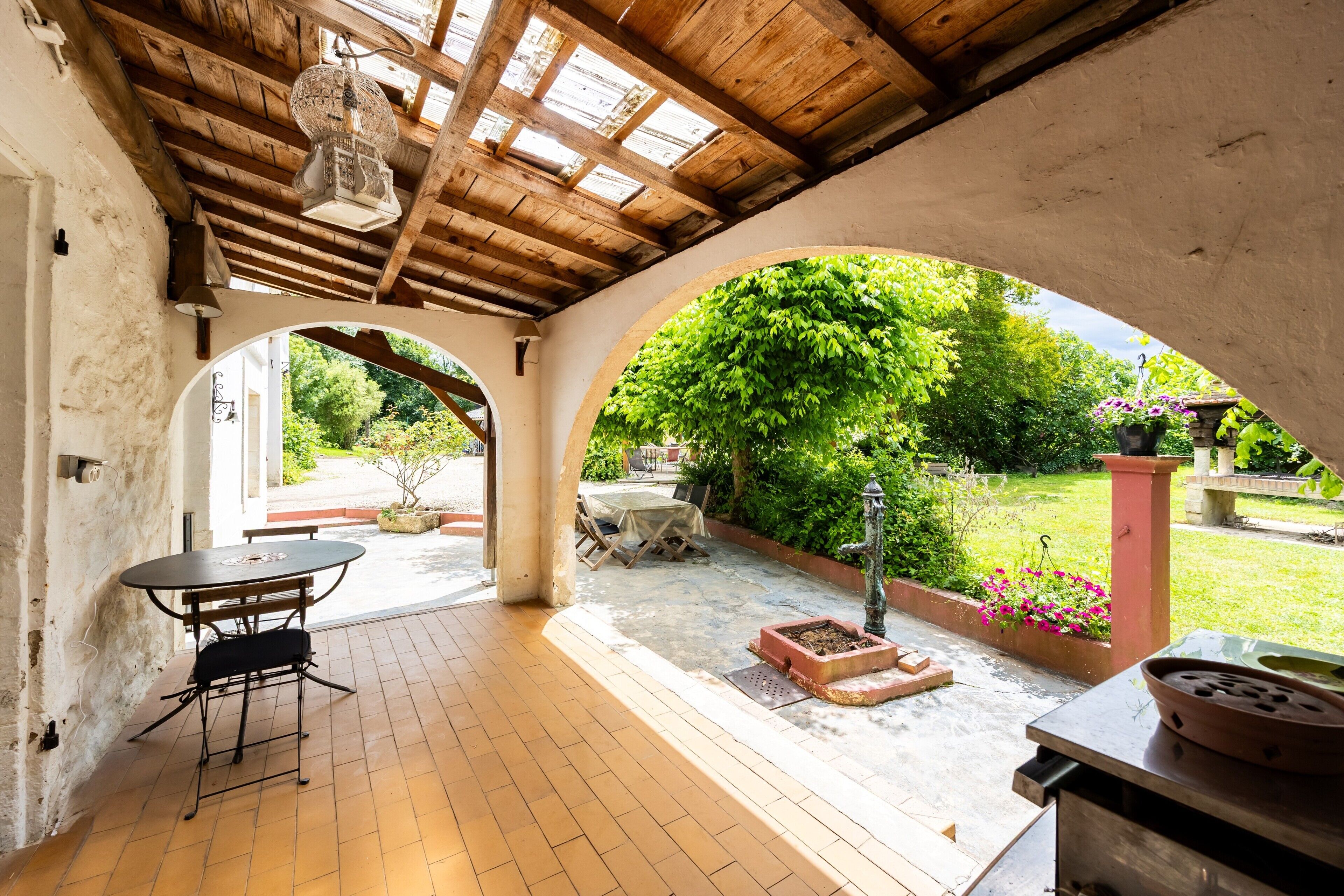 Eine Terrasse im Freien mit Tisch und Stühlen, einer hängenden Lampe und Blick auf einen Garten.