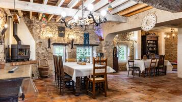 A rustic dining area with stone walls, wooden beams, and a fireplace.
