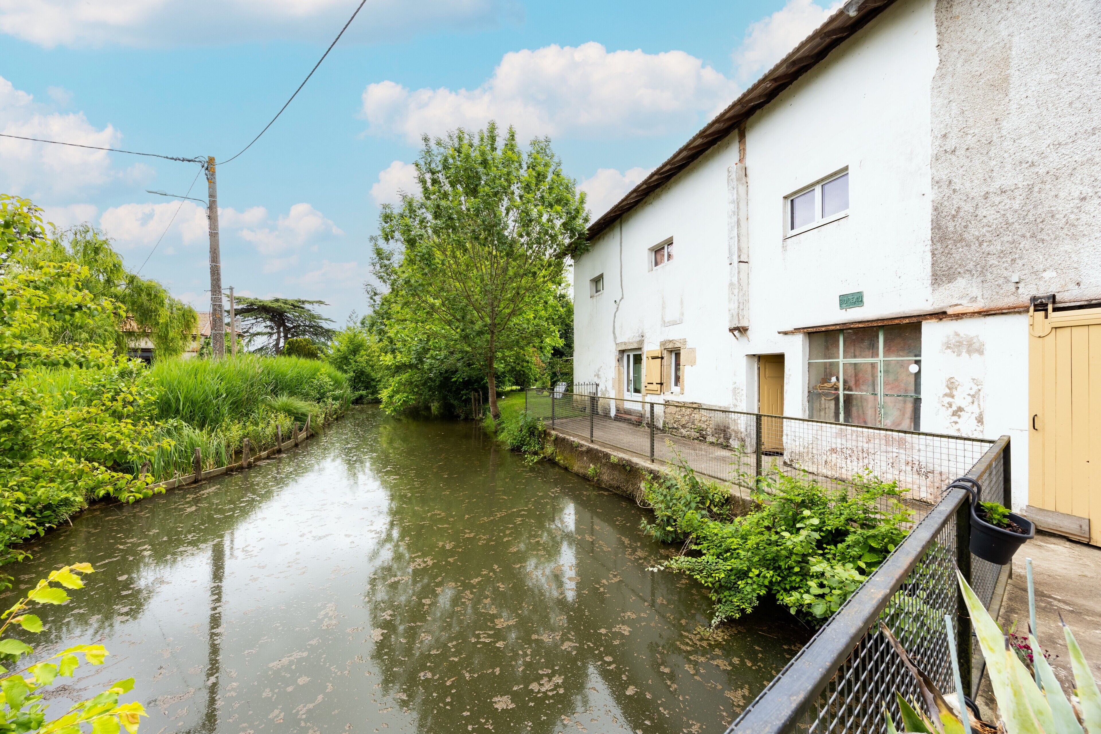 Un étroit canal bordé de verdure et un bâtiment blanc avec une porte marron.
