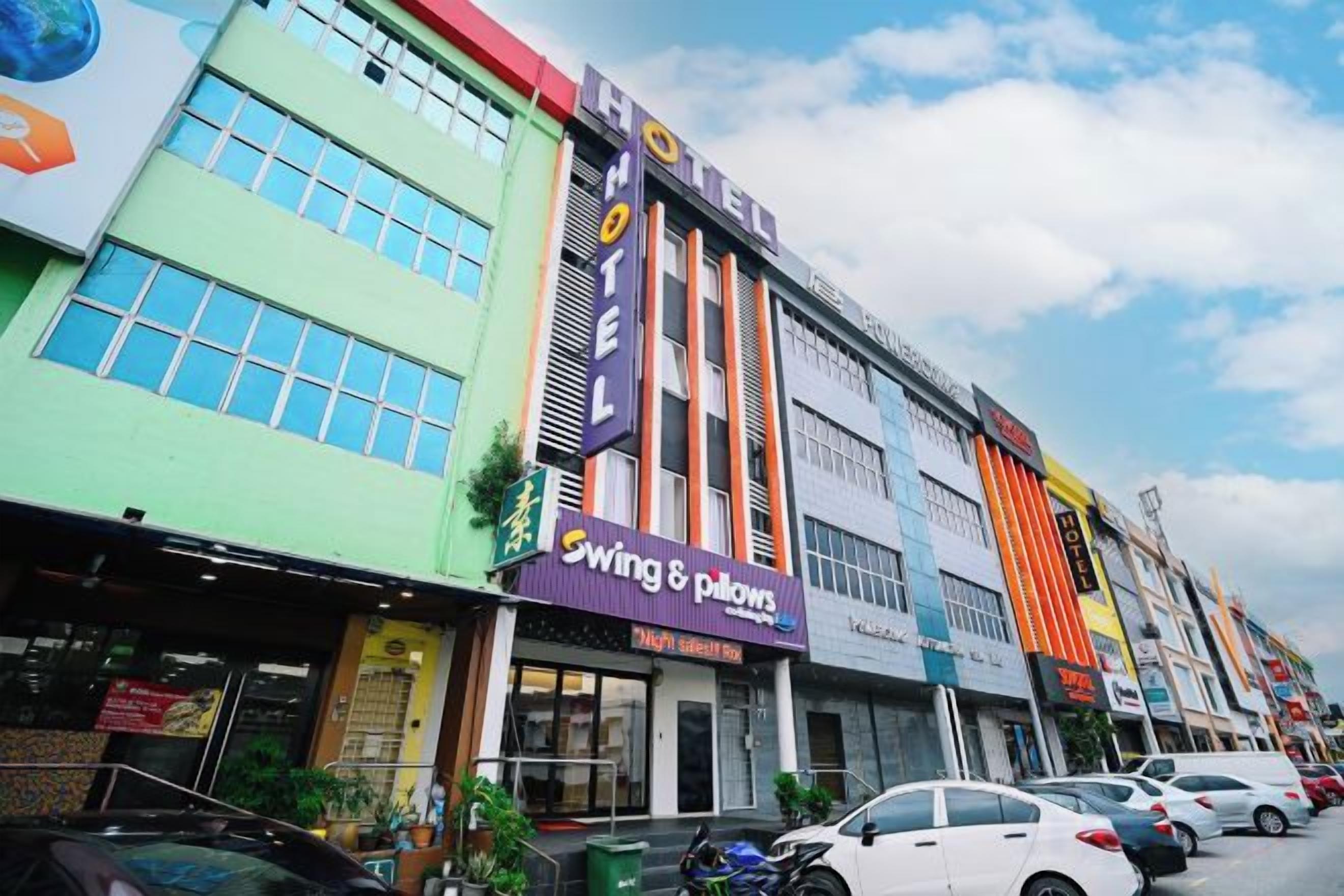 Een hotel met een kleurrijke gevel, een winkel met schommels en kussens, en een parkeerplaats met auto's.