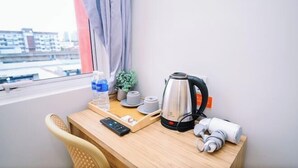 Ein Hotelzimmer mit Holzschreibtisch, Wasserkocher, Wasserflasche, Fernbedienung, kleiner Pflanze und einem Vorhangfenster.
