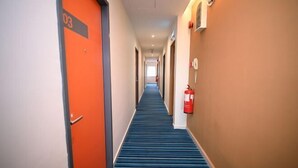 Ein Hotelkorridor mit blauem Teppich, orangefarbenen Türen und einem Feuerlöscher an der Wand.