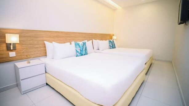 Ein Hotelzimmer mit einem großen Bett, Nachttischen, einem hölzernen Kopfteil und einem an der Wand befestigten Fernseher.