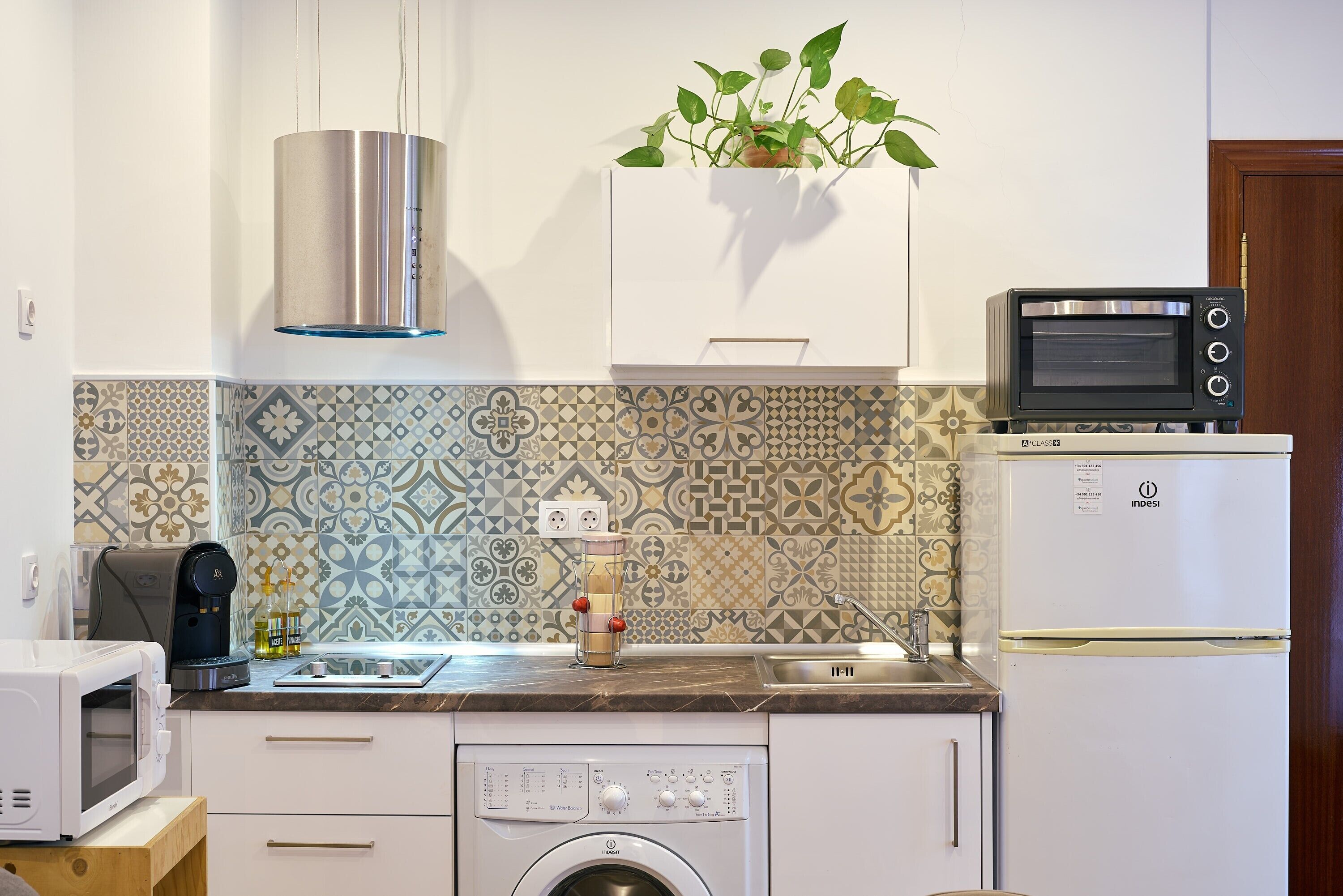 A kitchen with a washing machine, a microwave, a toaster oven, and a refrigerator.