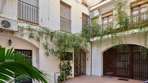 Un patio con paredes de ladrillo blanco, una reja de metal y plantas en macetas.