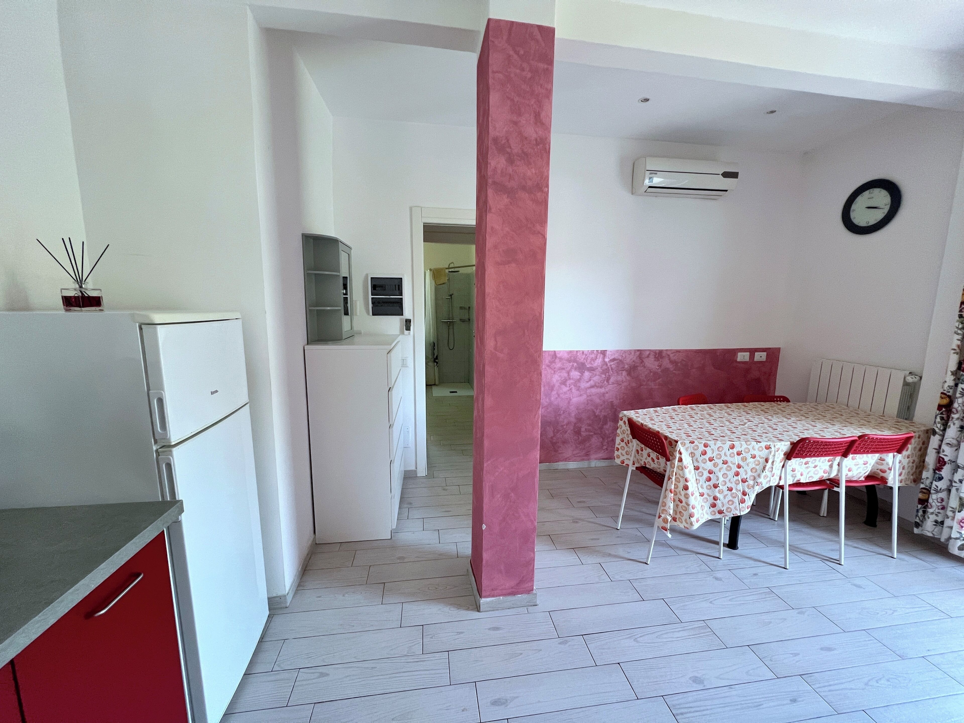 Cocina compacta con refrigerador, alacena pequeña y microondas.  Comedor con mesa y sillas, y zona de ducha con piso de baldosas.