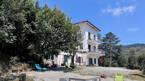 A two-story building with a balcony, surrounded by trees and a gravel area with outdoor furniture. - VILLA TIGULLIO (Chiavari)
