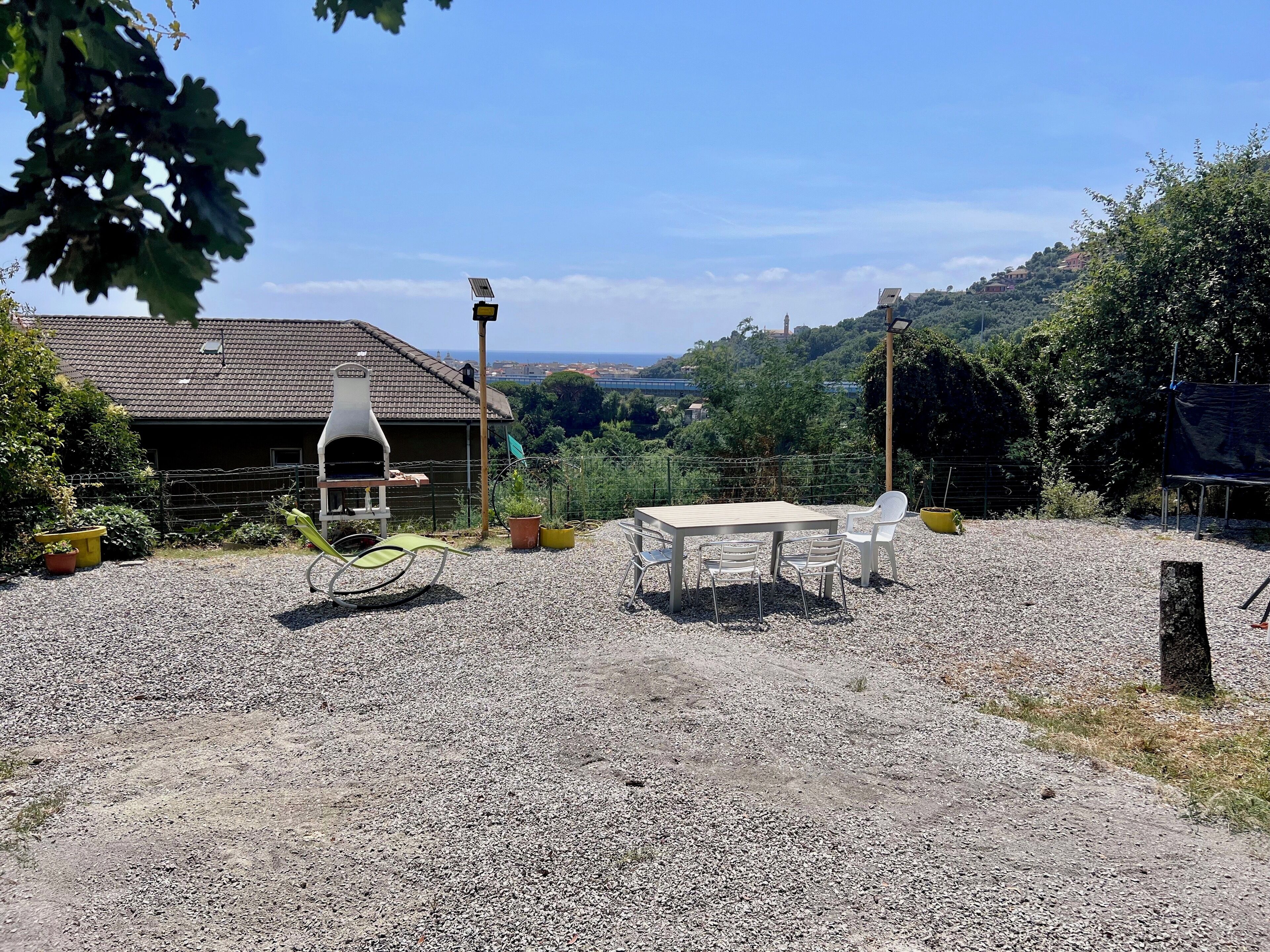 Eine gepflasterte Terrasse mit Tisch und Stühlen, einem Grill und Blick auf eine Hügellandschaft mit Häusern.