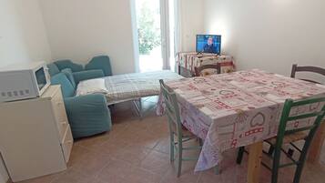 A small room with a bed, a table with a tablecloth, a television, and a microwave.