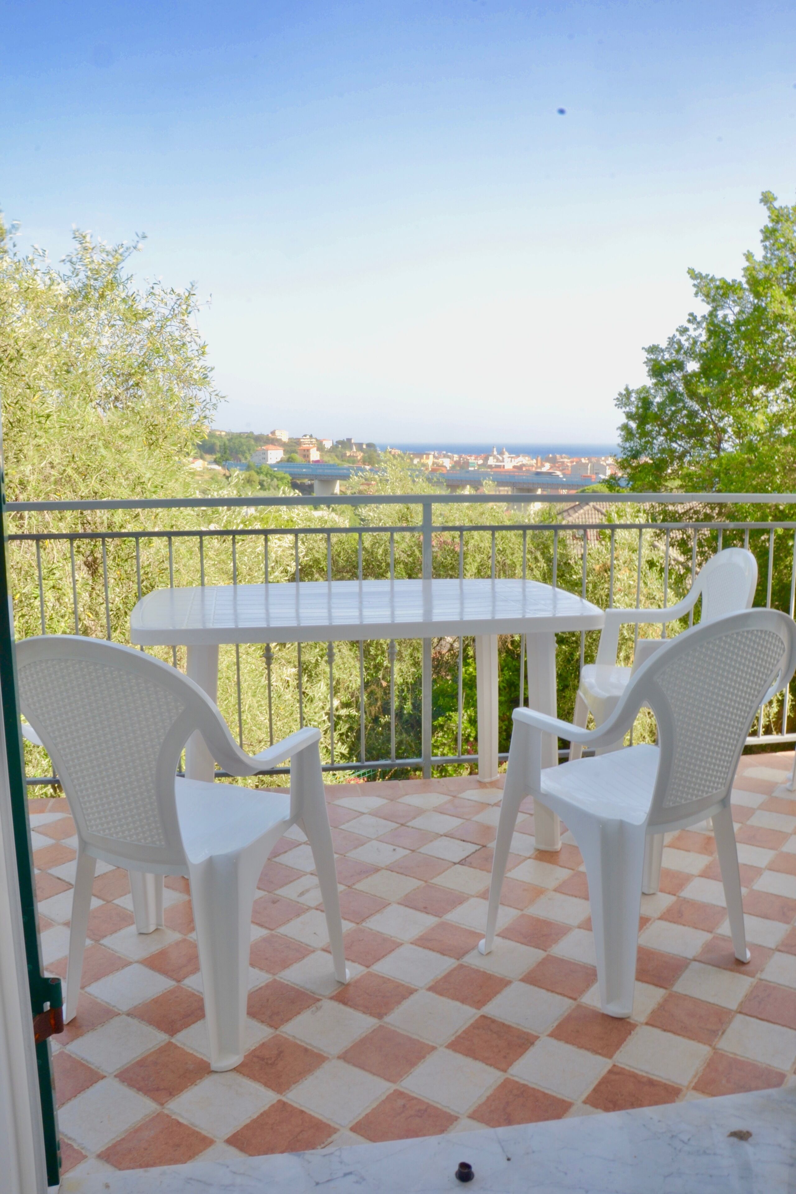 A balcony with a checkered floor, white chairs, and a table.