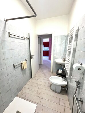 Un baño con baldosas grises, un lavamanos blanco, un inodoro, un perchero para toallas y una zona de ducha.