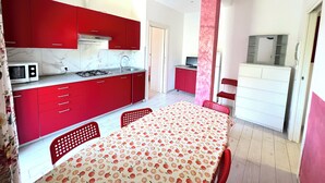 A compact kitchen with red cabinets, a microwave, and a dining area with a table and chairs. - VILLA TIGULLIO (Chiavari)