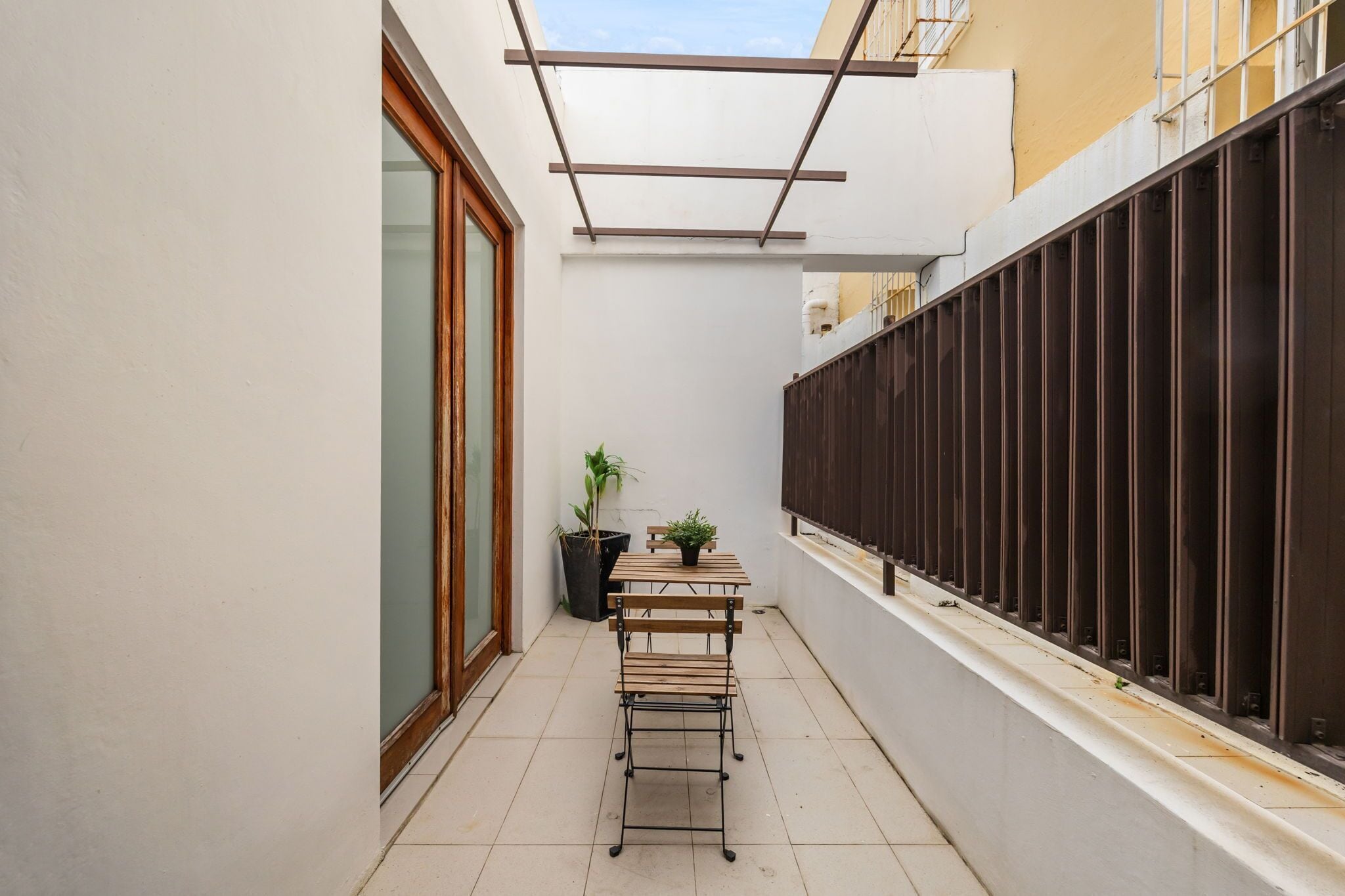 A narrow outdoor corridor with a wooden bench, a table, and potted plants.