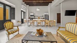 A spacious living area with a dining table and chairs, a coffee table with books, and a kitchen in the background.