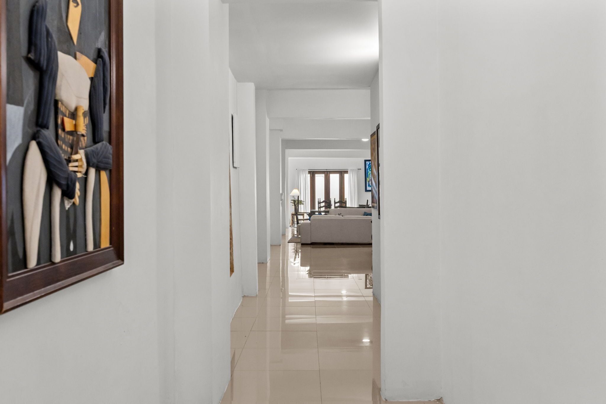 A hallway with a framed artwork on the left, leading to a living area with a sofa and a coffee table.