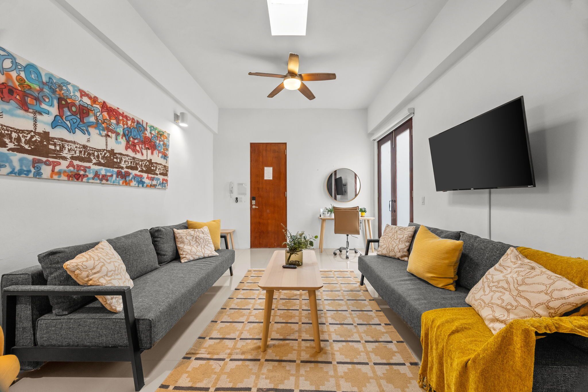 A modern living room with two sofas, a coffee table, a ceiling fan, a flat-screen TV, and a wall with graffiti art.