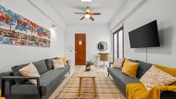 A modern living room with two sofas, a coffee table, a ceiling fan, a flat-screen TV, and a wall with graffiti art.