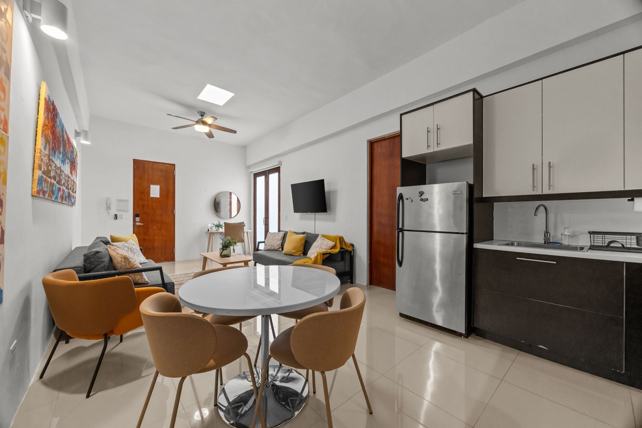 A modern living space with a dining area, kitchen, and a ceiling fan.
