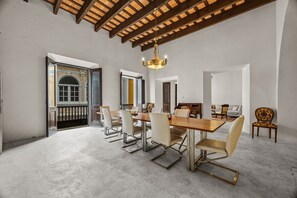 A spacious dining area with a high ceiling and exposed beams, a chandelier, and a view through an open door. - La Estadía (San Juan)