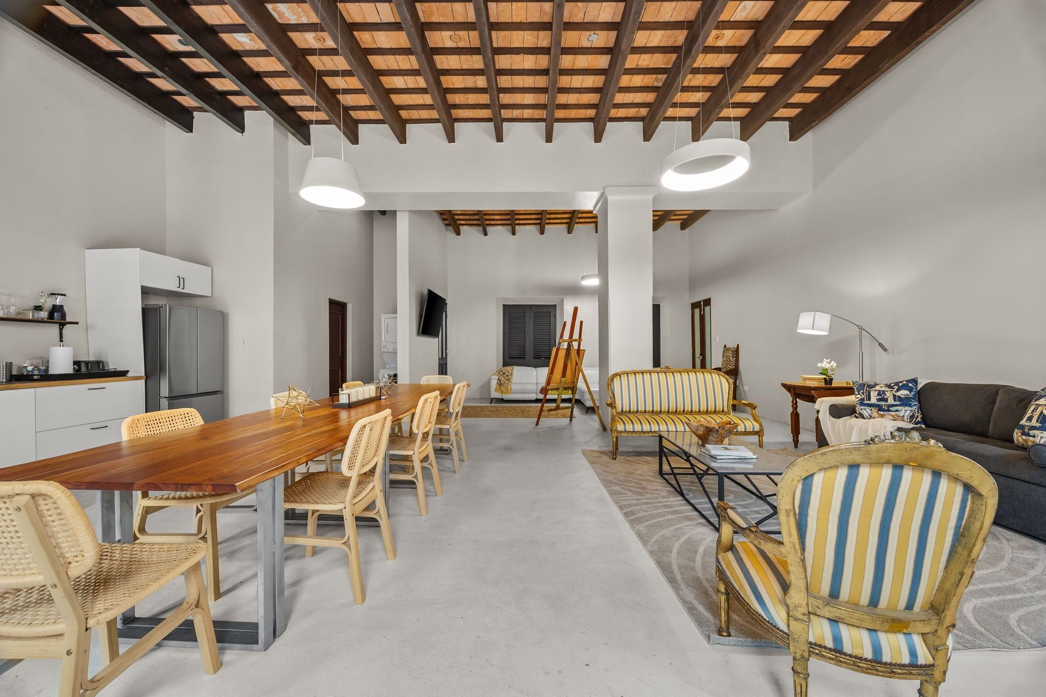 A spacious living area with a wooden dining table, wicker chairs, a sofa, and a painting easel.