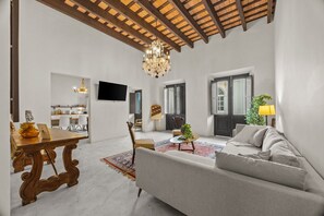 A spacious living room with a high ceiling, a chandelier, a sofa, a coffee table, and a dining area with a table and chairs. - La Estadía (San Juan)