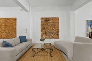 A modern living room with a sofa, armchair, coffee table, and abstract wall art. - La Estadía (San Juan)