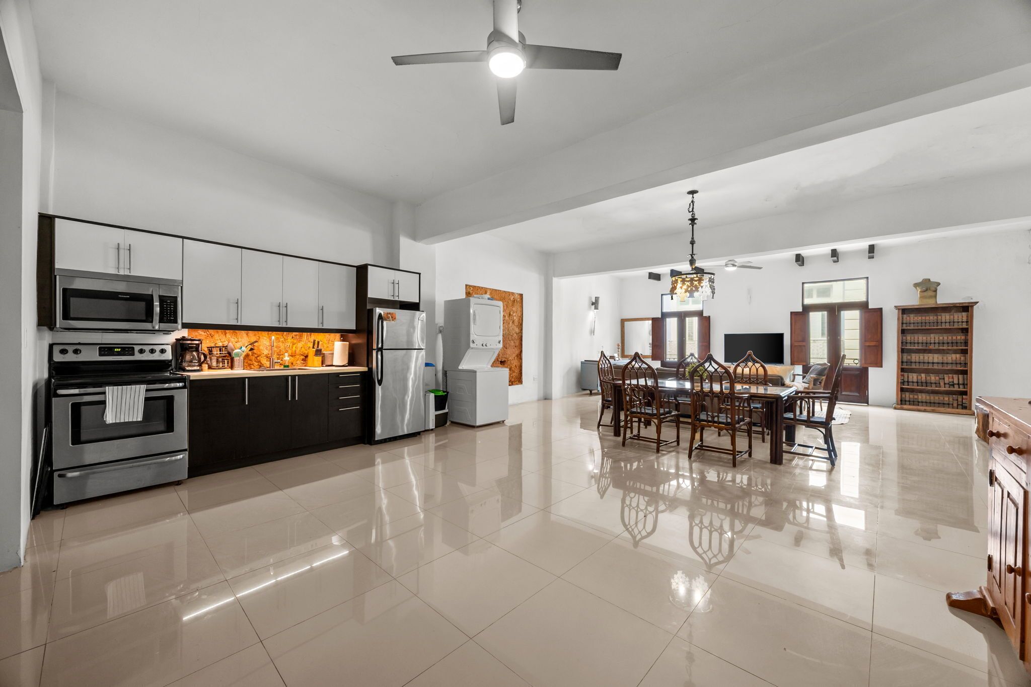 A modern kitchen with stainless steel appliances, a dining area with wooden chairs, and a large mirror on the wall.